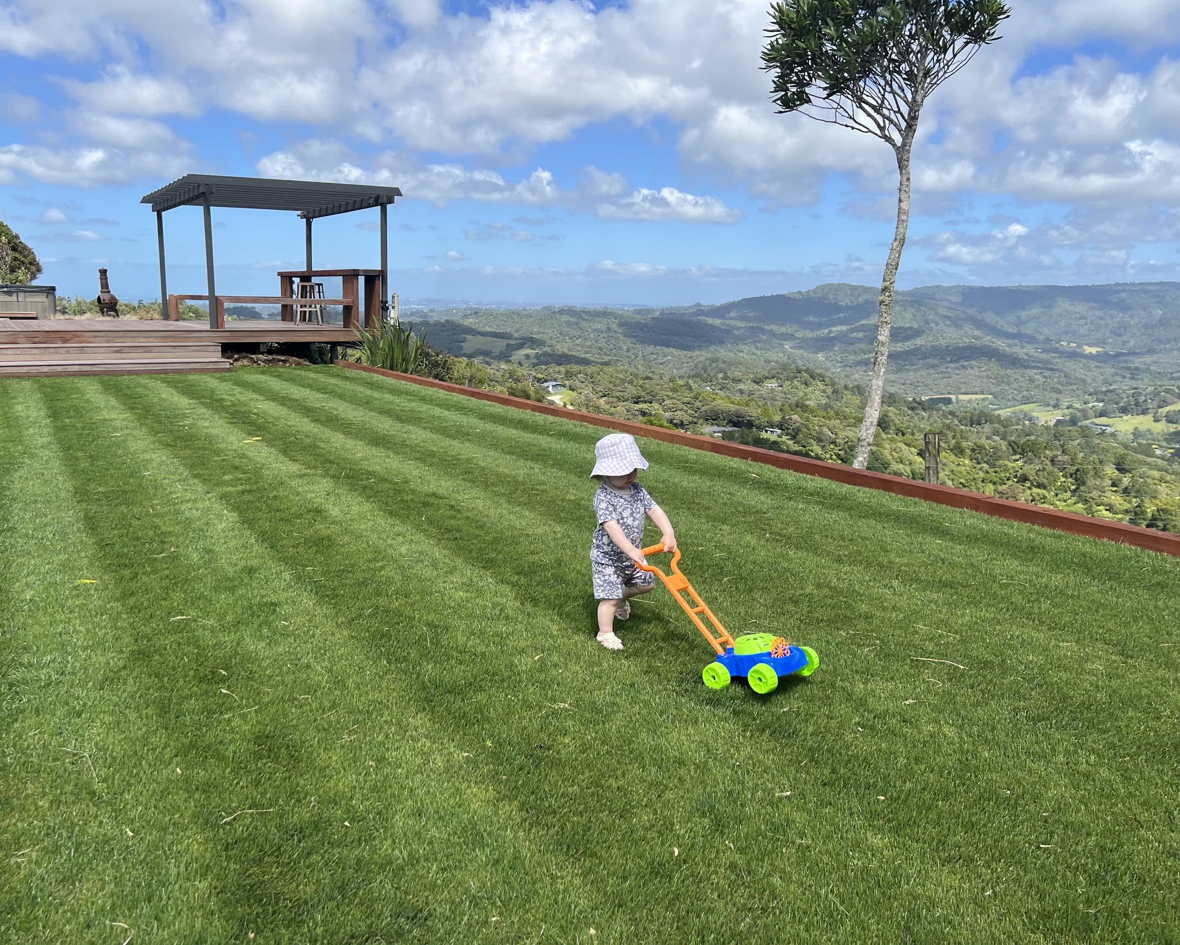 Josh's toddler pushing a toy lawn mower across a freshly striped lawn